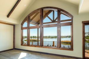 Great room looking out onto a beautiful view of the lake. Large fixed glass windows and exposed wood rafters.